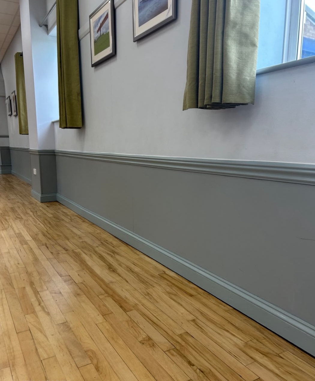 Refreshed woodwork at Sharnbrook Village Hall with grey-painted panelling, mouldings and skirting alongside a wooden floor.