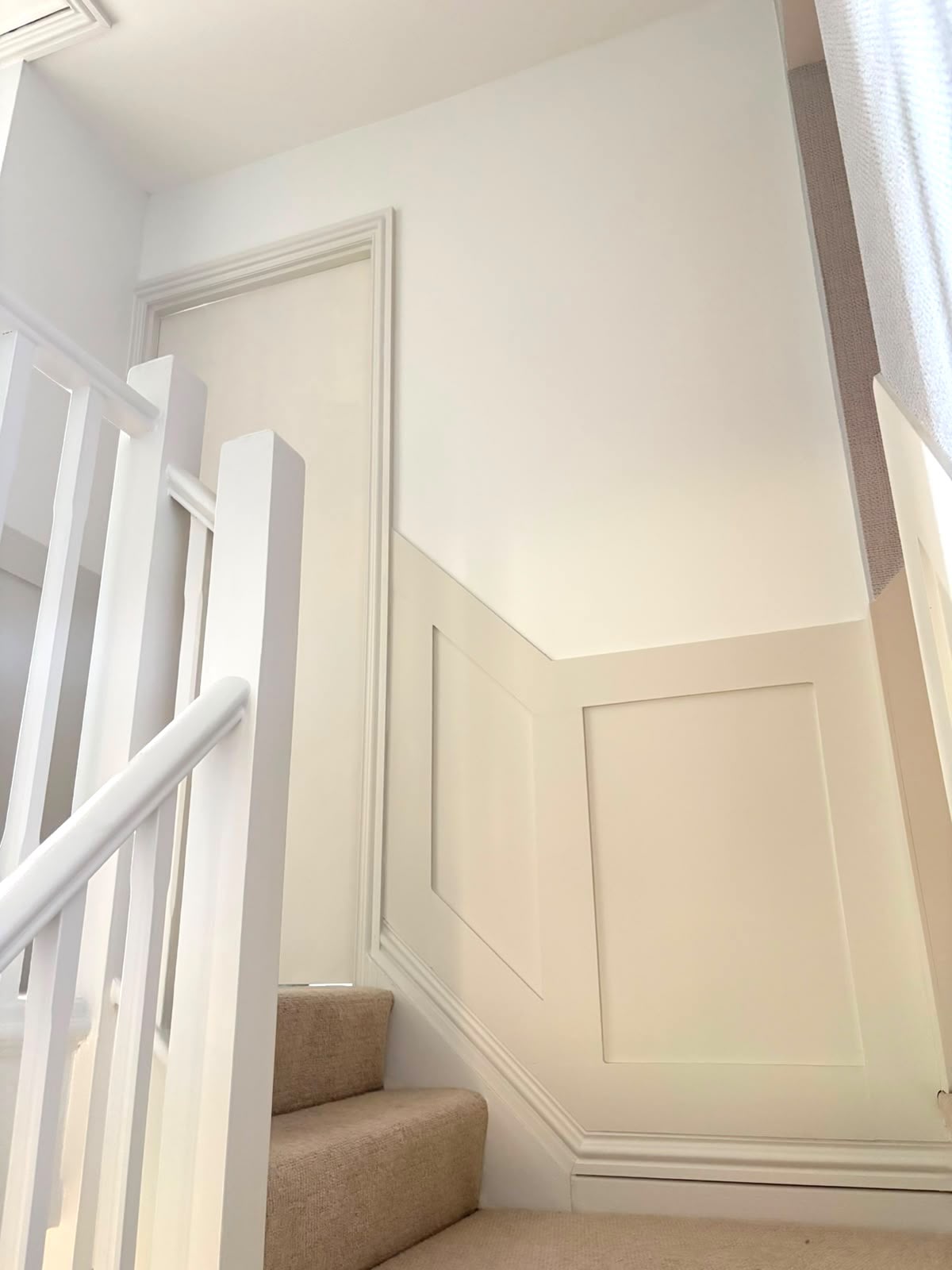 Freshly painted hallway and landing in Renhold with cream wall panelling, white staircase spindles and handrail.